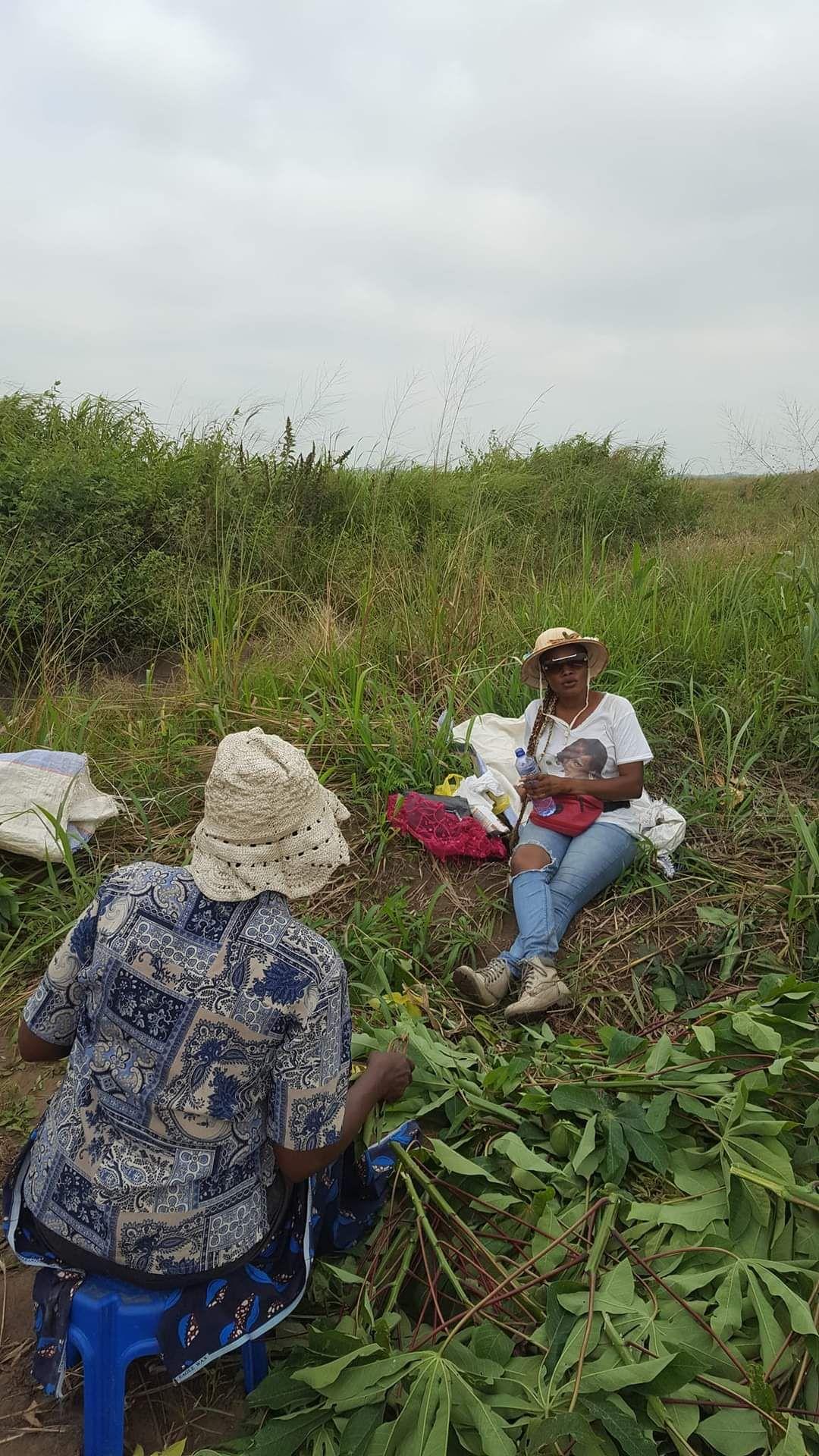 Two people sitting in a grassy field, one holding a water bottle, surrounded by harvested leaves.